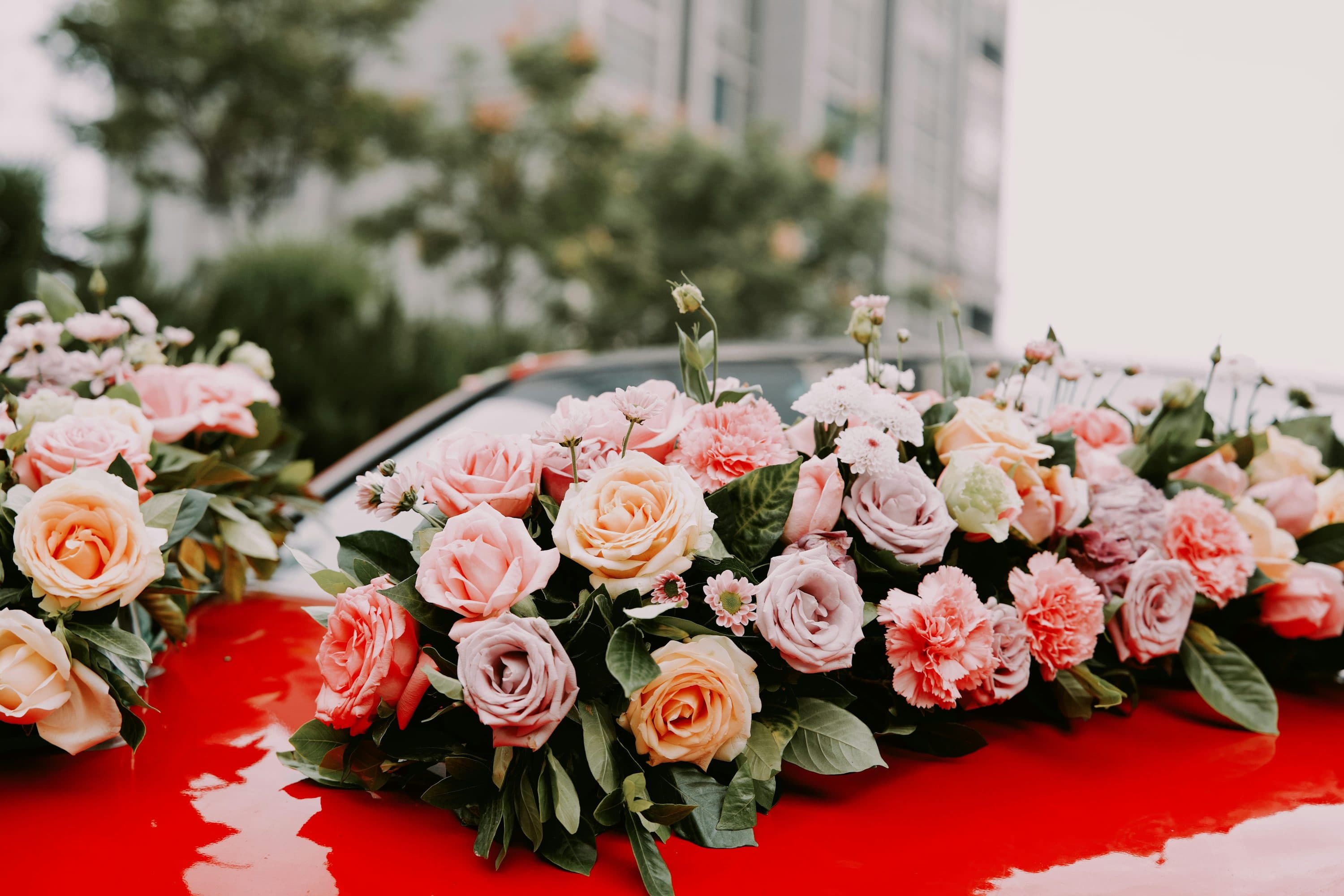 Pink and white flowers arranged on the hood of a red wedding car