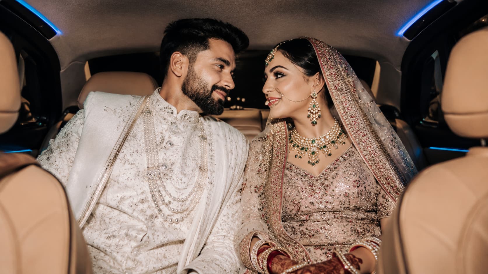 Indian bride and groom seated together inside a luxury wedding car